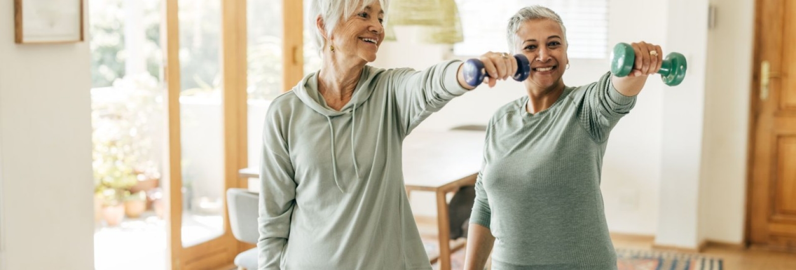 Zwei ältere Frauen, die zu Hause Krafttraining betreiben und einen aktiven sowie gesunden Lebensstil pflegen.