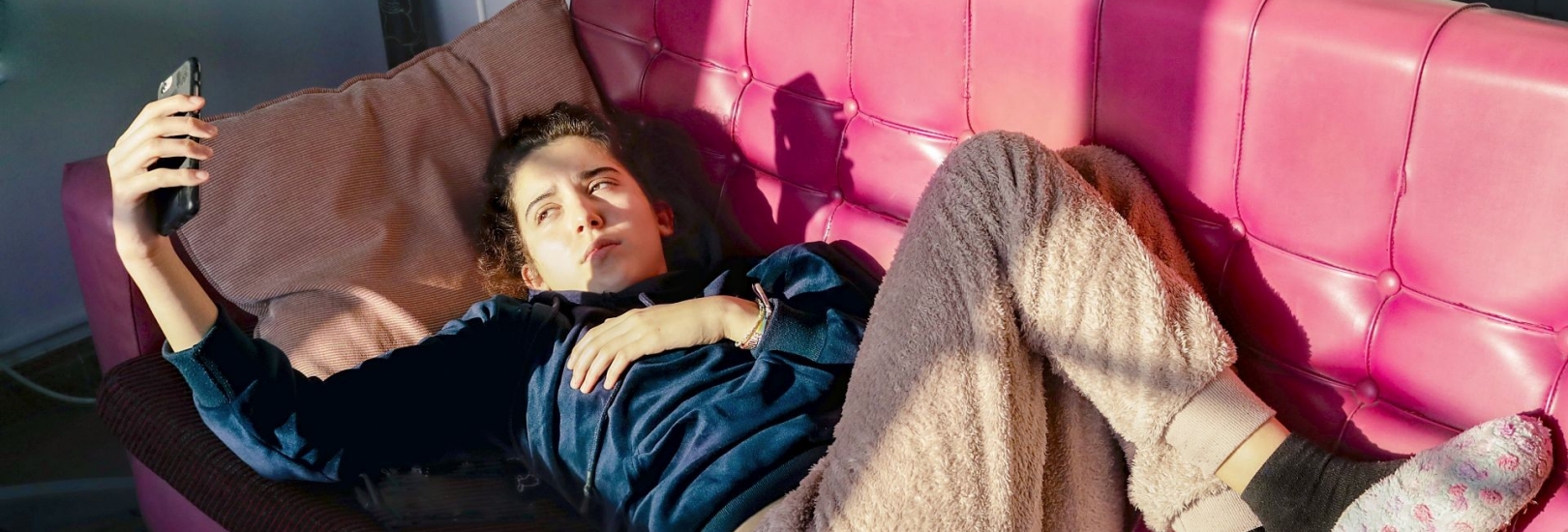 Teenage Girl laying on a red sofa, looking at her mobile phone,  during quarantine