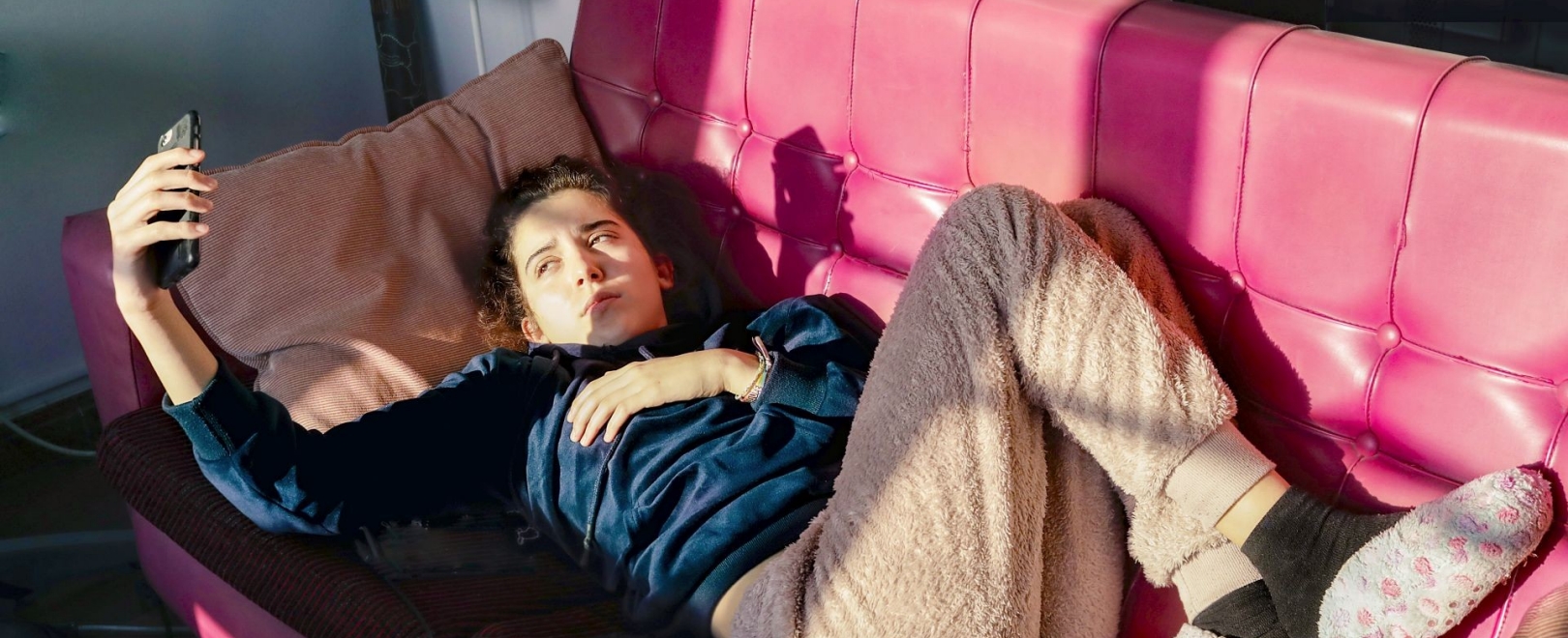 Teenage Girl laying on a red sofa, looking at her mobile phone,  during quarantine