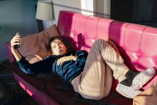 Teenage Girl laying on a red sofa, looking at her mobile phone,  during quarantine