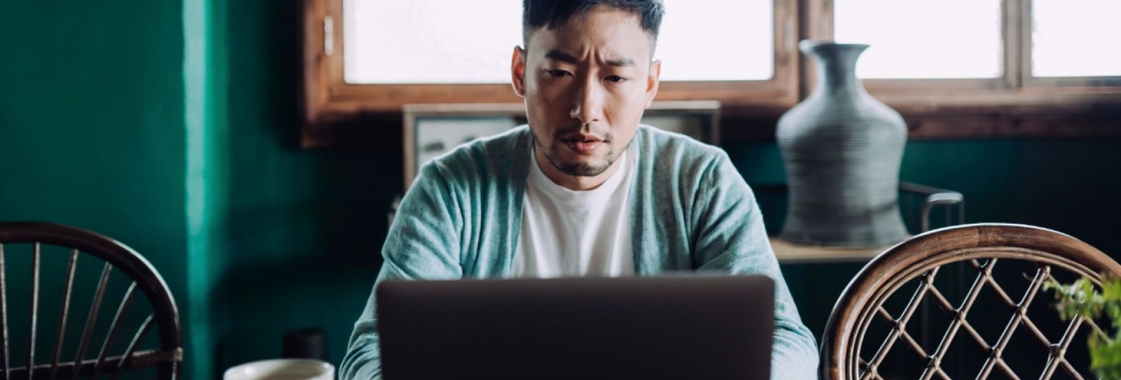 Ein junger asiatischer Mann sitzt mit besorgter Mine vor einem Laptop.