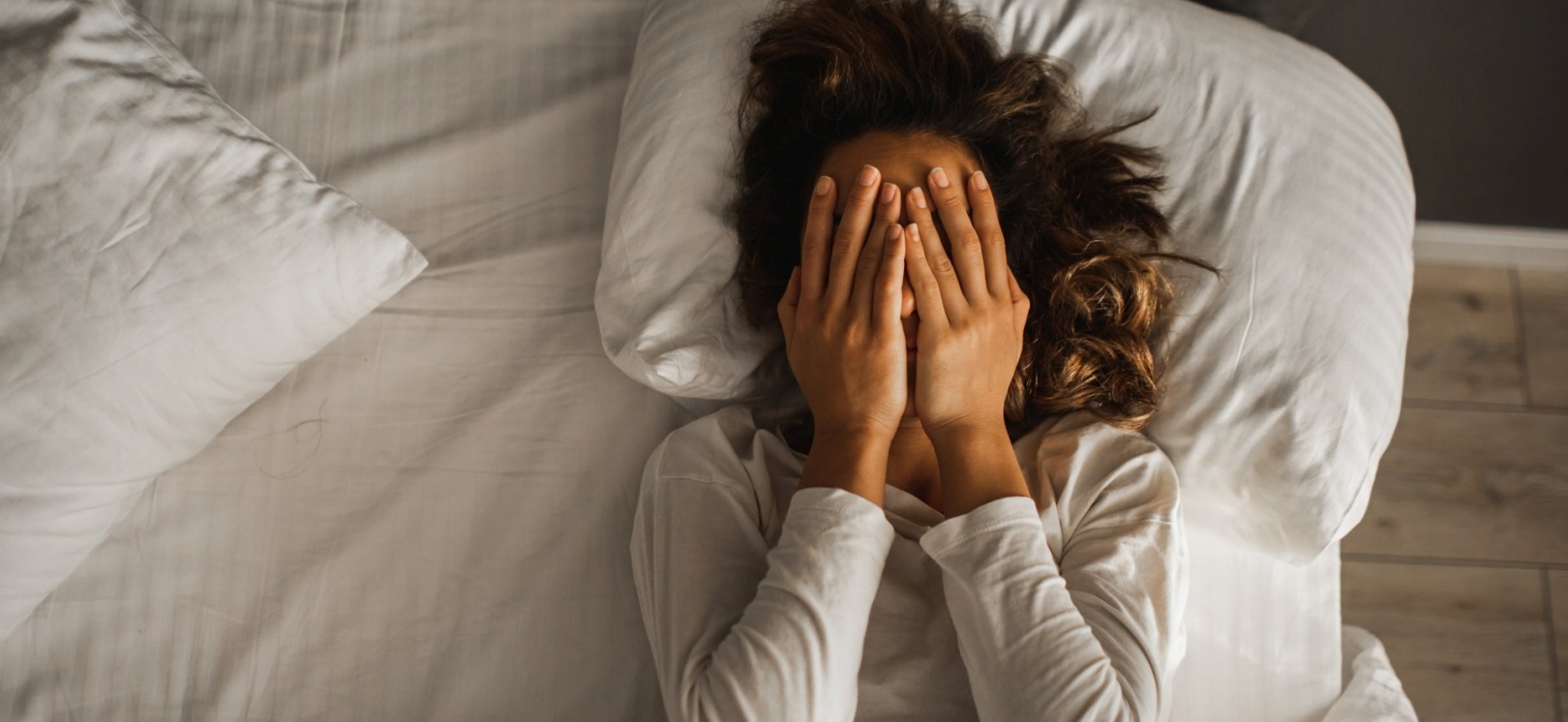 Eine Frau liegt im gestresst im Bett und schlägt die Hände vor ihrem Gesicht zusammen.
