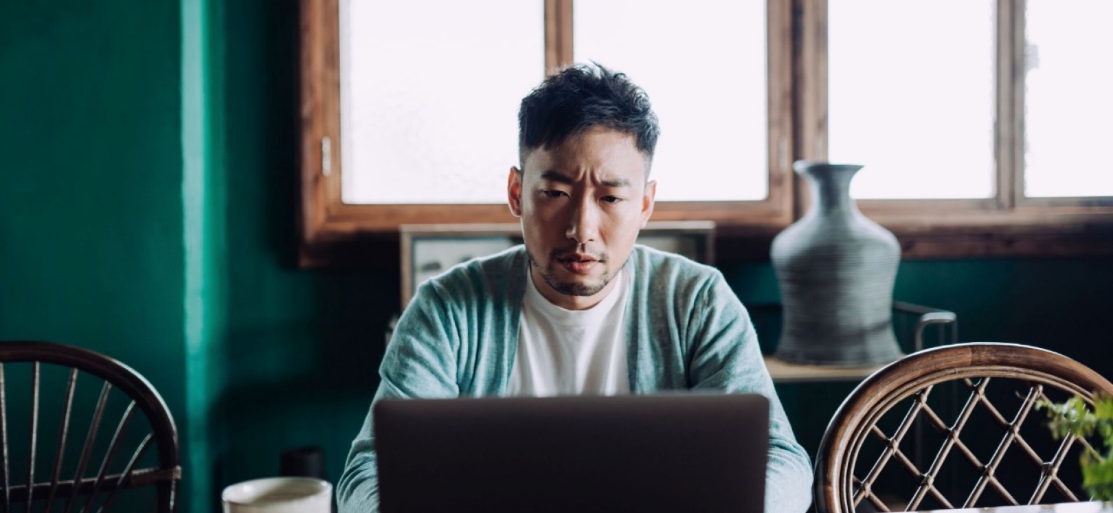 Ein junger asiatischer Mann sitzt mit besorgter Mine vor einem Laptop.