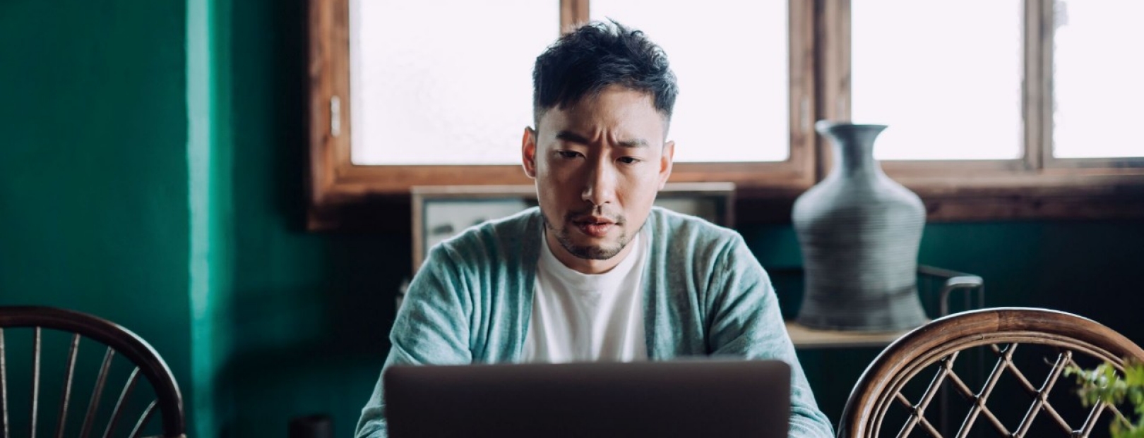 Ein junger asiatischer Mann sitzt mit besorgter Mine vor einem Laptop.