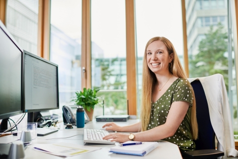 Frau am Arbeitsplatz schaut lächelnd in die Kamera