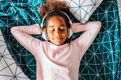 Ein kleines afroamerikanisches Mädchen genießt ihre Freizeit zu Hause und hört Musik. Sie hat die Augen geschlossen.