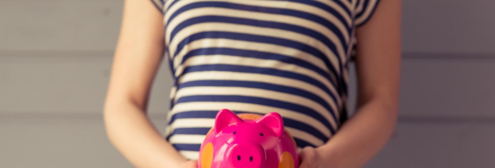 Eine schwangere Frau hält ein Sparschwein in der Hand vor ihren Bauch.
