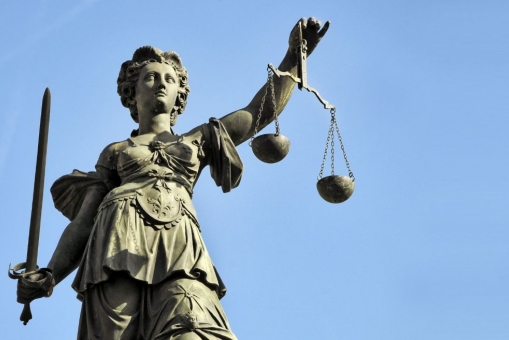 Abgebildet ist die Gerechtigkeitsgöttin Justizia als Bronze Statur. 