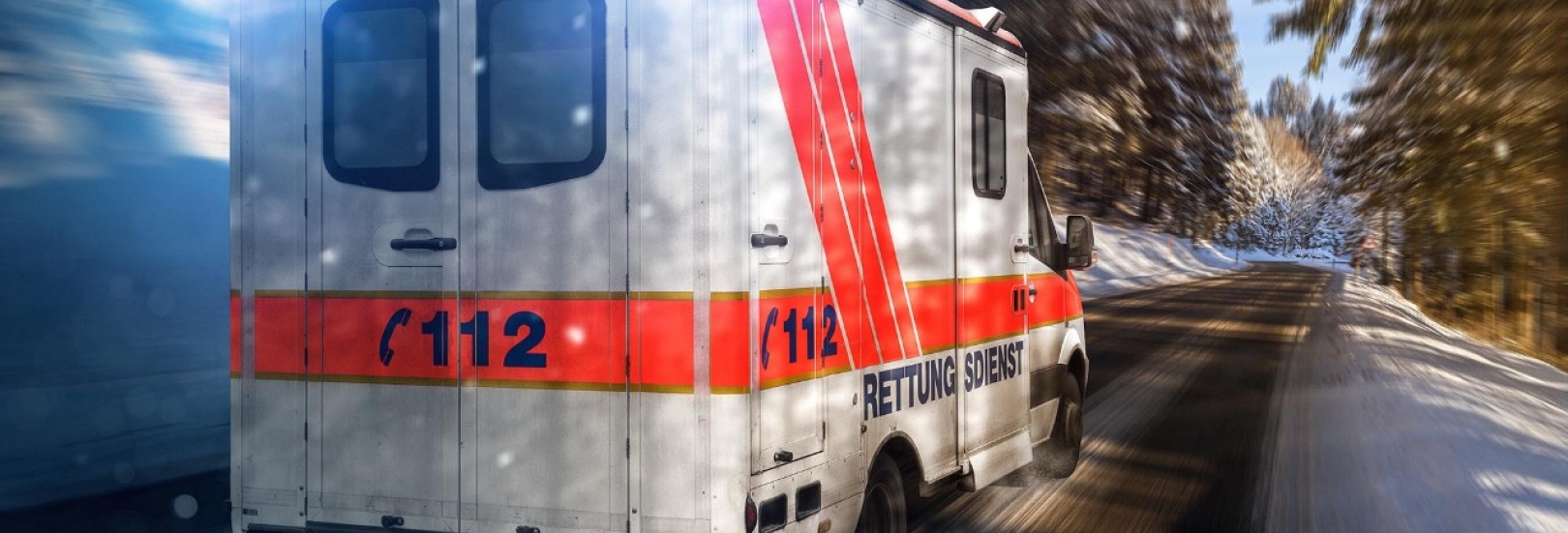 Ein Krankenwagen fährt schnell mit Blaulicht auf einer leicht mit Schnee bedeckten Straße.