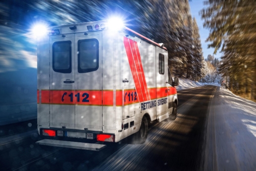 Ein Krankenwagen fährt schnell mit Blaulicht auf einer leicht mit Schnee bedeckten Straße.