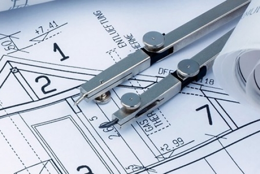 Abgebildet ist ein Bauplan eines Architekten mit einem Taschenrechner. Zusätzlich liegt ein Zirkel und ein Zollstock auf dem Bauplan.