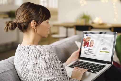 Eine Frau sitzt auf dem Sofa im Wohnzimmer und schaut auf ihren Laptop. Sie hat die Seite vom Online Pflegecoach der KKH geöffnet.
