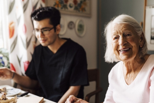 Eine Seniorin sitzt mit einem jüngeren Mann am Tisch und essen gemeinsam Kuchen.