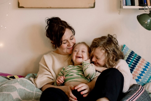 Eine Mutter kuschelt und albert mit ihren Kindern im Bett.