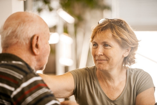 Eine Tochter besucht ihren älteren Vater in Pflegeeinrichtung. Sie lächelt.