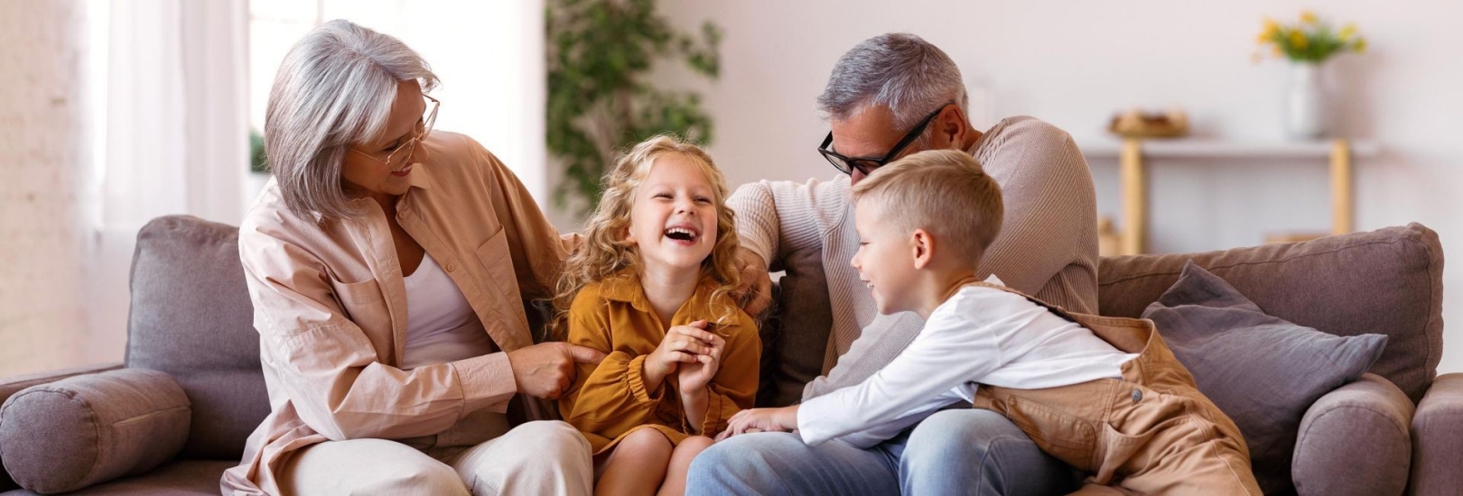 Zwei junge Kinder spielen mit ihren Großeltern auf dem Sofa.