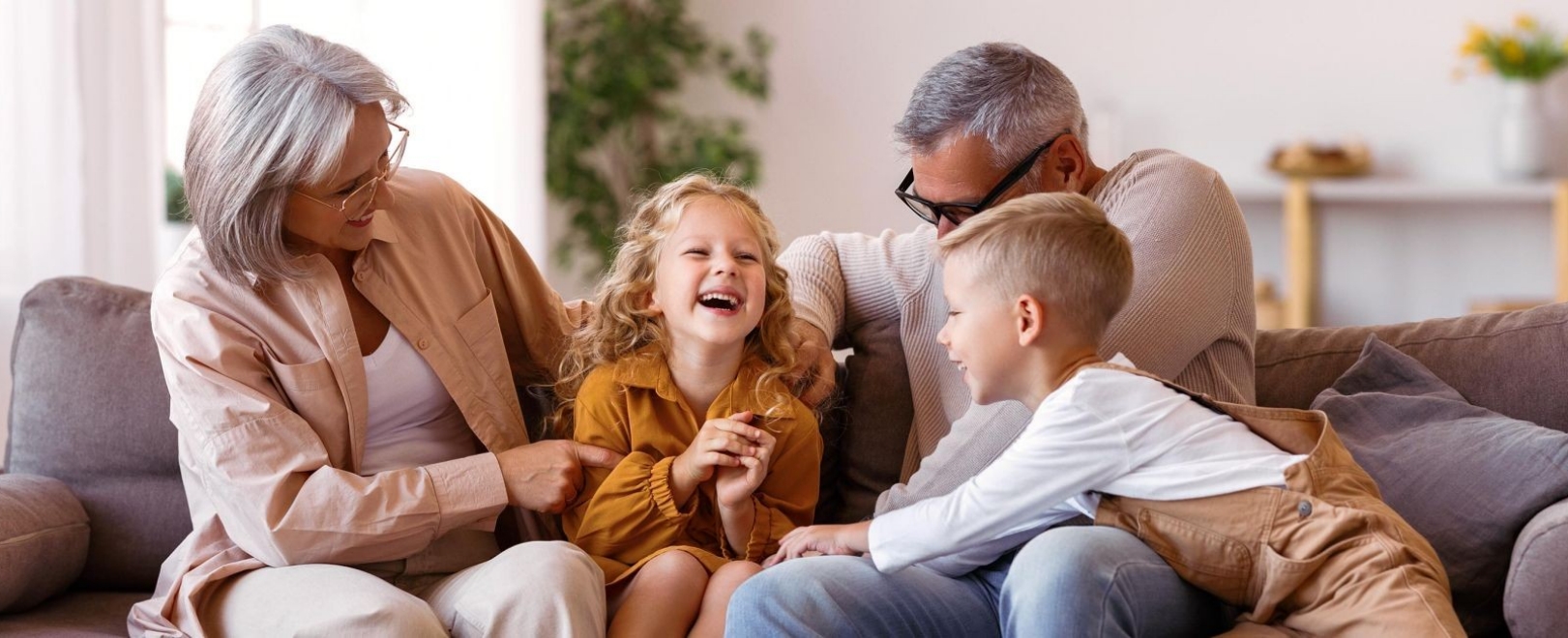 Zwei junge Kinder spielen mit ihren Großeltern auf dem Sofa.